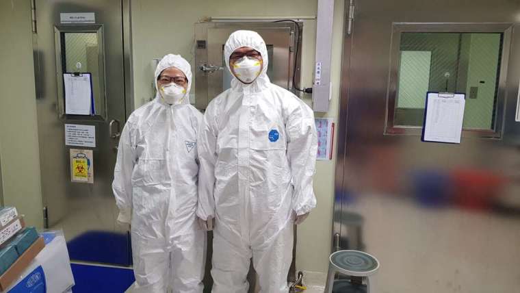 林宜玲實驗室同仁在 P3 實驗室前合影。P3 實驗室的工作人員必須穿著實驗衣，而且穿、脫順序都有嚴格的 SOP，並配合定期訓練。 圖│林宜玲