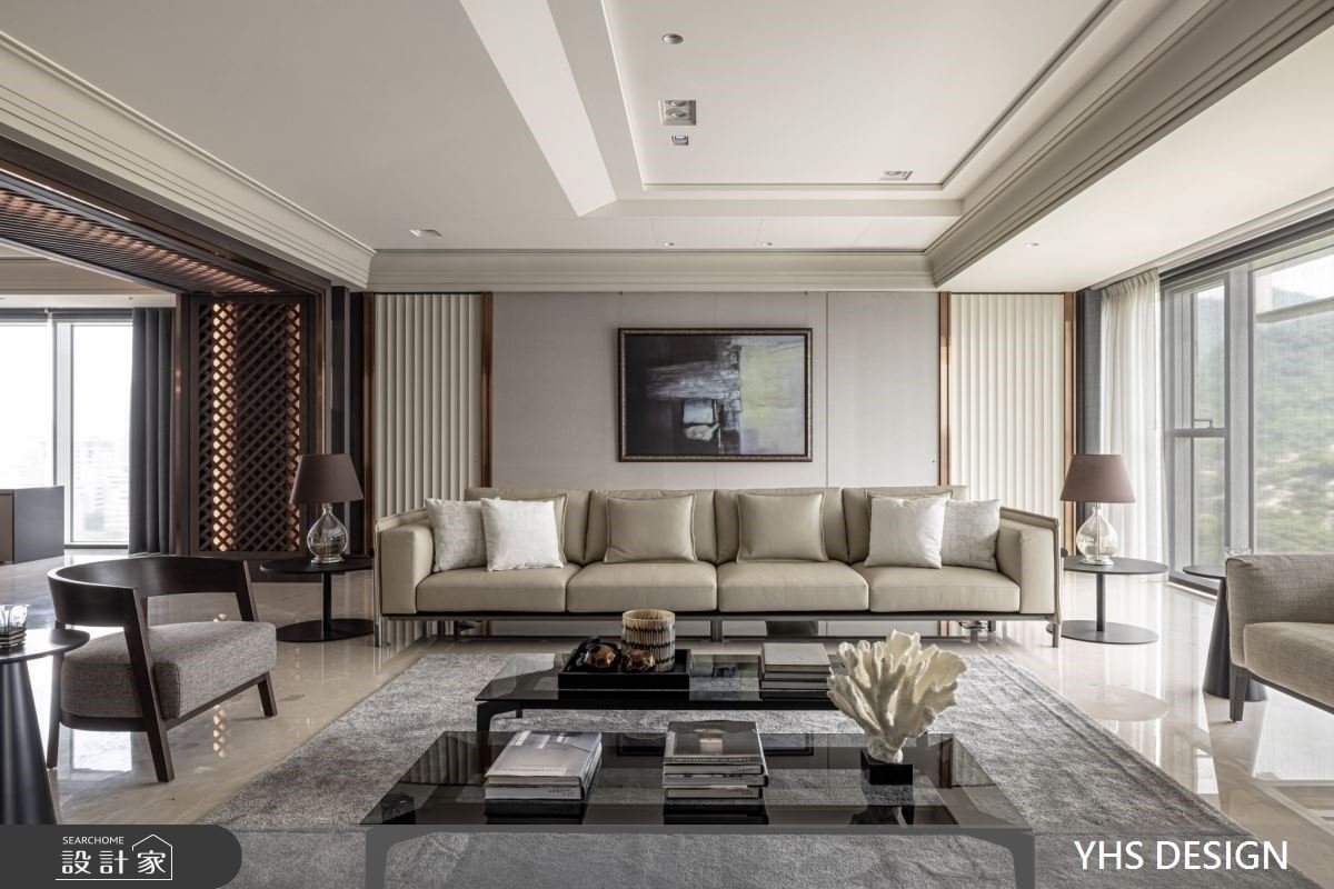 明亮舒適的大型客廳，以米白色皮革長沙發和對稱的背牆設計，延伸豪宅的開闊氣勢軸寬，並綴入金屬線性和深色的家具細節，呈現精緻大方的空間個性。