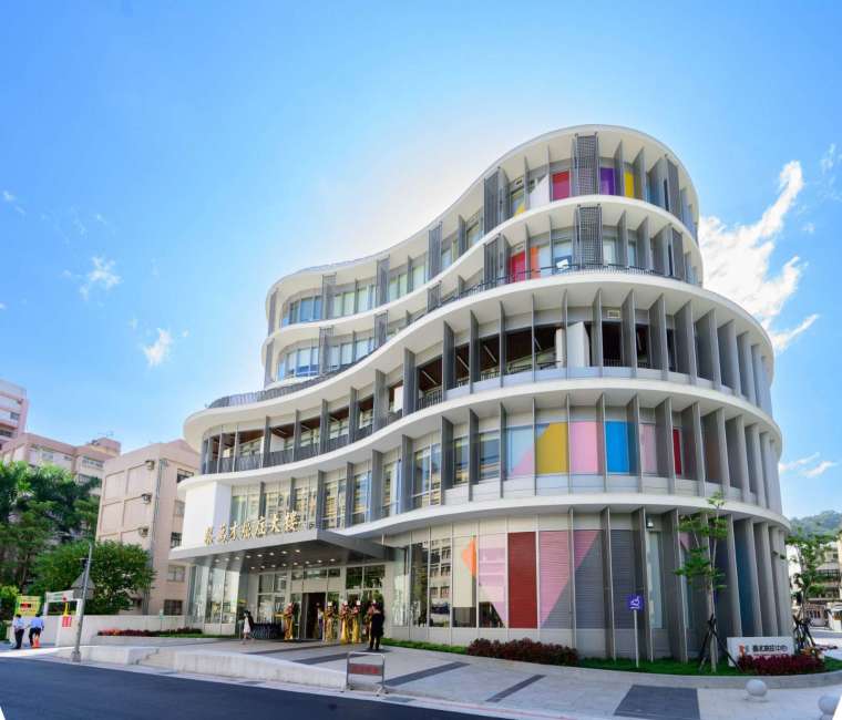 蔡萬才癌症大樓以微笑曲線的造型、搭配生態綠園，12 種彩色玻璃為不同癌症的代表色，傳達關懷與抗癌的意象。（圖：富邦金控提供）
