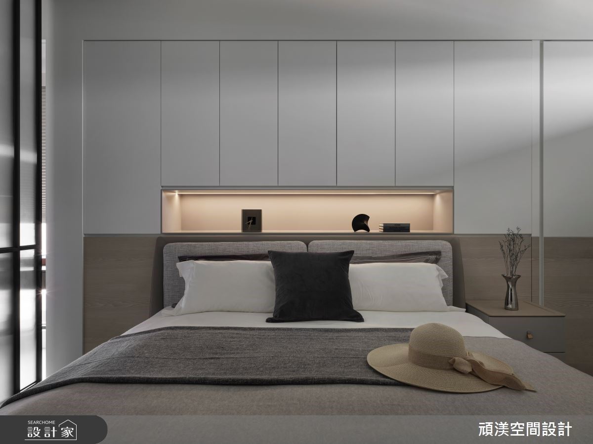 以白木灰色調帶出臥室沉靜的質感，與右方衛浴門形成完整的面，中段設有床頭置放區符合使用需求。