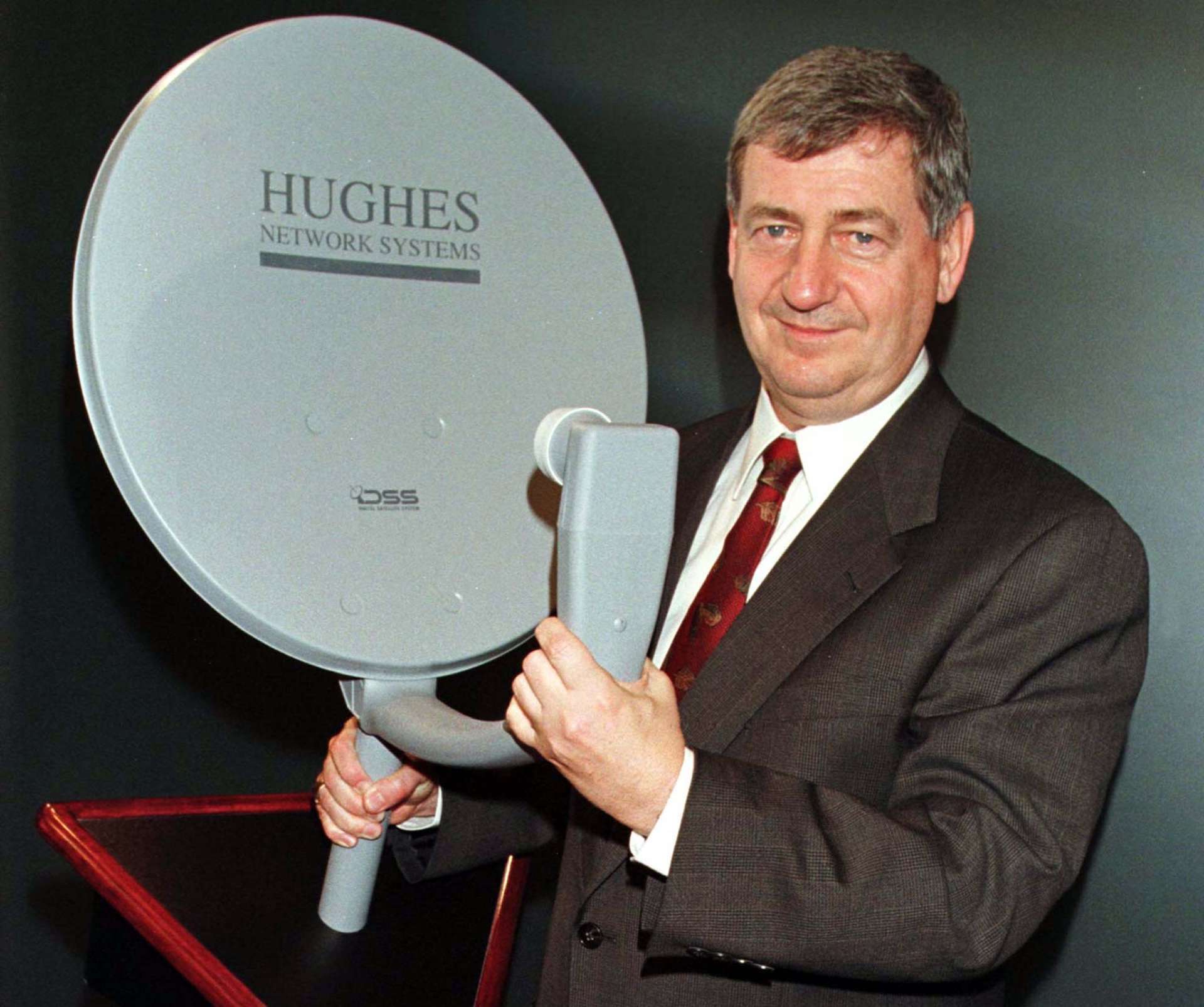 Hughes Electronics前董事長兼執行長Michael T. Smith於公司總部展示Hughes Network Systems數位衛星電視（DSS）接收天線。DSS系統可將數位電視訊號直接傳送至消費者家中。Reuters/TPG